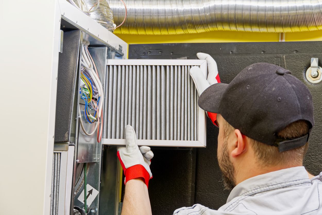 HVAC service technician changing dirty air filter in the central ventilation system. Change filter in rotary heat exchanger recuperator. Air duct ventilation system maintenance for clean air. See Less